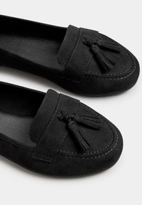 Svarta mockaloafers med dekorativa tofsar, med en slät yta, sömnadsdetaljer och en rundad form.