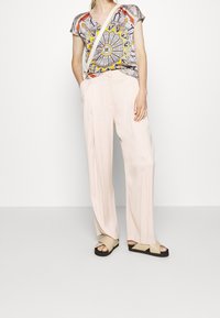 Blouse multicolore avec un motif floral, associée à un pantalon large rose clair et des sandales noires avec des brides beiges.