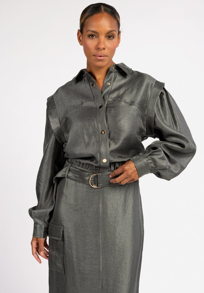 Grey metallic shirt dress with oversized sleeves, button closure, and a matching belt featuring a circular metal buckle. Smooth texture.