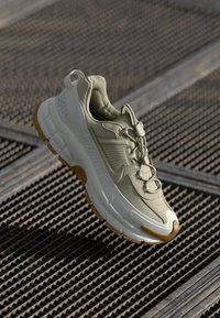 Ljusgröna sportskor med texturerad ovandel, rundad tå och tjock vit och brun gummisula. Har snörningssystem och logotypdetaljer.