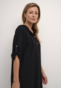 Rochie neagră cu glugă, fabricată dintr-un material ușor, având deschidere cu nasturi, mâneci pliate și detaliu cu șnur.