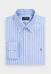 Camisa de botones de manga larga de color azul claro con rayas blancas, doblada cuidadosamente. Presenta un cuello, puños abotonados y un pequeño logo bordado.