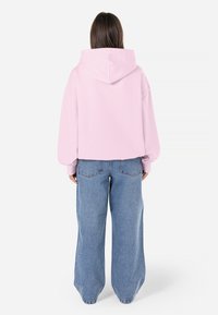 Moletom rosa cropped com capuz, corte solto, combinado com jeans azuis de perna larga. Textura suave com punhos canelados e bolsos traseiros.