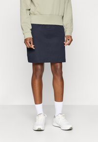 Saia de algodão azul-marinho, até ao joelho, com uma cintura elástica. Combinada com um sweatshirt cinza claro e ténis brancos.