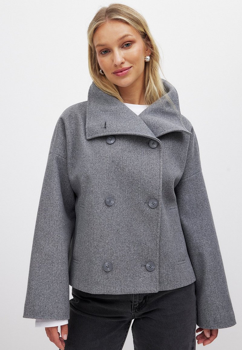 Grå ullblendad jacka med en dubbelknäppt design, stor krage och två framfickor. Har grå knappar och vida ärmar.