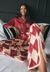 Set aus rotem Satin mit Schwäne-Muster und cremefarbenen Akzenten. Das Oberteil hat eine Knopfleiste und die weit geschnittenen Hosen haben eine ausgestellte Form.