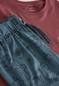 Tamsiai raudonas medvilninis džemperis su apvalia iškirpte, derinamas su tamsiai mėlynomis kelnėmis, kuriose juodu pavaizduotas kavos tematikos raštas. Abi dalys yra laisvo silueto.