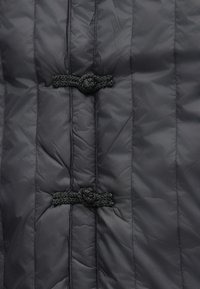 Giacca a piuma nera con texture trapuntata, due chiusure a cordoncino intrecciato e finitura lucida. Design leggero e isolato.