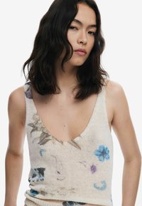Débardeur en tricot de couleur crème clair, avec des motifs floraux bleu et violet, un décolleté en V profond et une texture douce.