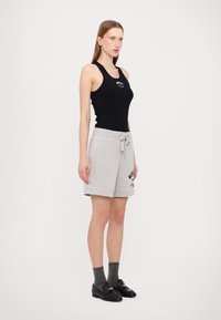 Juodas juostuotas tank top'as su grafika, derinamas su pilkais šortais su raišteliu ir atspaudo akcentais. Modelis dėvi pilkas kojines ir juodas loafer tipo batus.