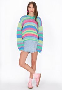 Maglione lavorato a maglia oversize colorato con strisce orizzontali in rosa, blu e verde. Abbinato a una gonna di jeans e sneakers rosa.