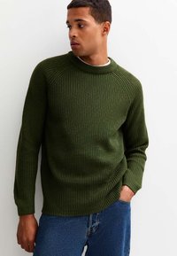 Mörkgrön ribbad tröja med hög krage, långa ärmar och figurnära passform. Texturen är stickad och skapar ett upphöjt mönster.