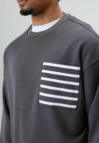 Gray sweatshirt featuring a striped pocket, made of soft fabric with a crew neckline and visible stitching details.