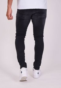 Jeans negros ajustados con un acabado desgastado, con bolsillos traseros cosidos. Combinados con zapatillas blancas con acentos azules.