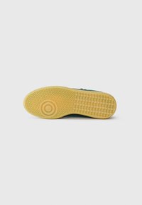 Baskets à semelle en caoutchouc avec une outsole jaune, présentant un motif de grip texturé et un dessus vert foncé avec un détail minimal.