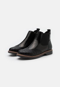 Black leather Chelsea boots with textured toe, smooth body, elastic side panels, and a brown stitched sole. Accent in heel area.