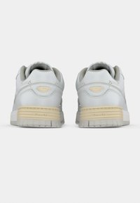 Baltos odinės sportbačiai suapvalintu priekiu, paminkštintu apykakle ir smėlio spalvos guminiu padu su tekstūruotu raštu bei subtiliu prekės ženklu ant kulno.