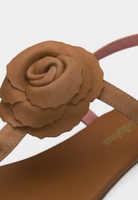 Καφέ σανδάλι με διακοσμητικό τριαντάφυλλο από δερμάτινη υφή στο λουράκι και καφέ πέλμα που ταιριάζει, σε λευκό φόντο.