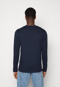 Camiseta de manga larga en color azul marino, fabricada en un tejido suave, con cuello redondo y corte recto, combinada con pantalones de mezclilla azul claro.