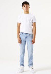 Weißes kurzärmeliges T-Shirt, kombiniert mit hellblauen Jeans und weißen High-Top-Sneakers. Die Jeans haben einen lässigen Sitz und eine subtile Ausbleichung.