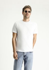 T-shirt bianco in cotone con maniche corte, scollatura rotonda e una texture morbida, abbinato a jeans in denim blu chiaro.