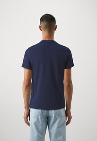Námořnická modrá bavlněná trička s krátkým rukávem; kulatý výstřih a jednoduchý design; hladká textura; nošené s světle modrými džínami.