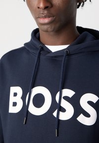 Sweatshirt navy com um grande logotipo branco "BOSS", com capuz regulável e tecido texturizado, projetado para um ajuste casual.