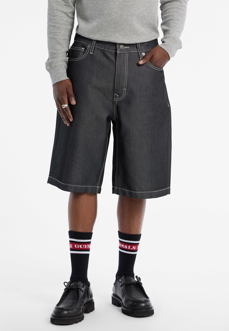 Shorts en denim bleu foncé avec des coutures blanches contrastantes, dotés d'une fermeture à bouton, de passants de ceinture et de poches latérales.