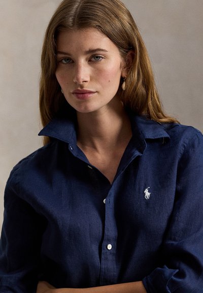 Marineblå lin-skjorte med knappestolpe, hvit brodert logo og lange ermer, med en avslappet passform og myk tekstur.