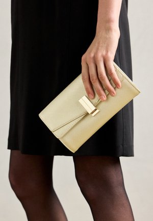 Beige teksturert clutch-lommebok med lukking av gullhardware, holdt i hånden, som viser sin rektangulære form og minimalistiske design.