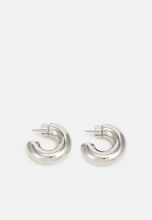 Orecchini a cerchio in tono argento con un design curvo e liscio, dotati di una superficie testurizzata e di un perno a vite per la chiusura.