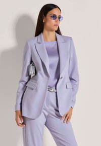 Lichtpaarse op maat gemaakte blazer met een satijnen afwerking, voorzien van twee voorzakken en een enkele knoopsluiting, gecombineerd met een bijpassend topje en broek.