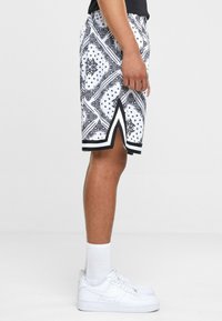 Black and white patterned shorts with a bandana design, featuring a side slit and black trim. Paired with white sneakers and socks.