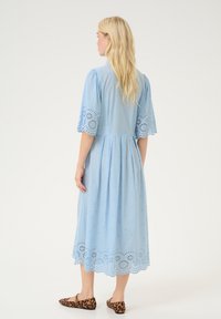 SvetloModra bombažna obleka z detajli broderie anglaise, kratkimi nagubanimi rokavi in krojem, ki sega pod kolena. Ujemajoči leopardasti balerinki.