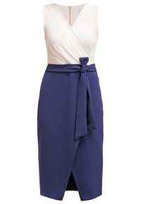 Robe portefeuille sans manches avec un haut crème et une jupe bleu marine. Elle possède un lien sur le côté et une fermeture éclair au dos. Tissu lisse avec une finition élégante.