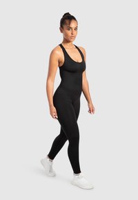 Zwarte sportieve body met een ronde hals en brede banden. Strakke pasvorm, gemaakt van soepele stof. Gecombineerd met witte sportschoenen.
