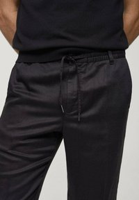 Black trousers with a smooth texture, elastic waistband, and adjustable drawstring. Features belt loops and a tailored fit.