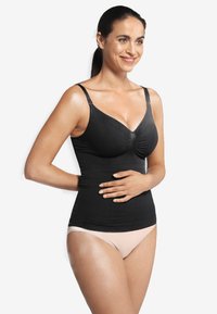 Svart stretchig linne med justerbara axelremmar, gathered bust-design och slät tygtextur. Bärs över ljusbeige underkläder.