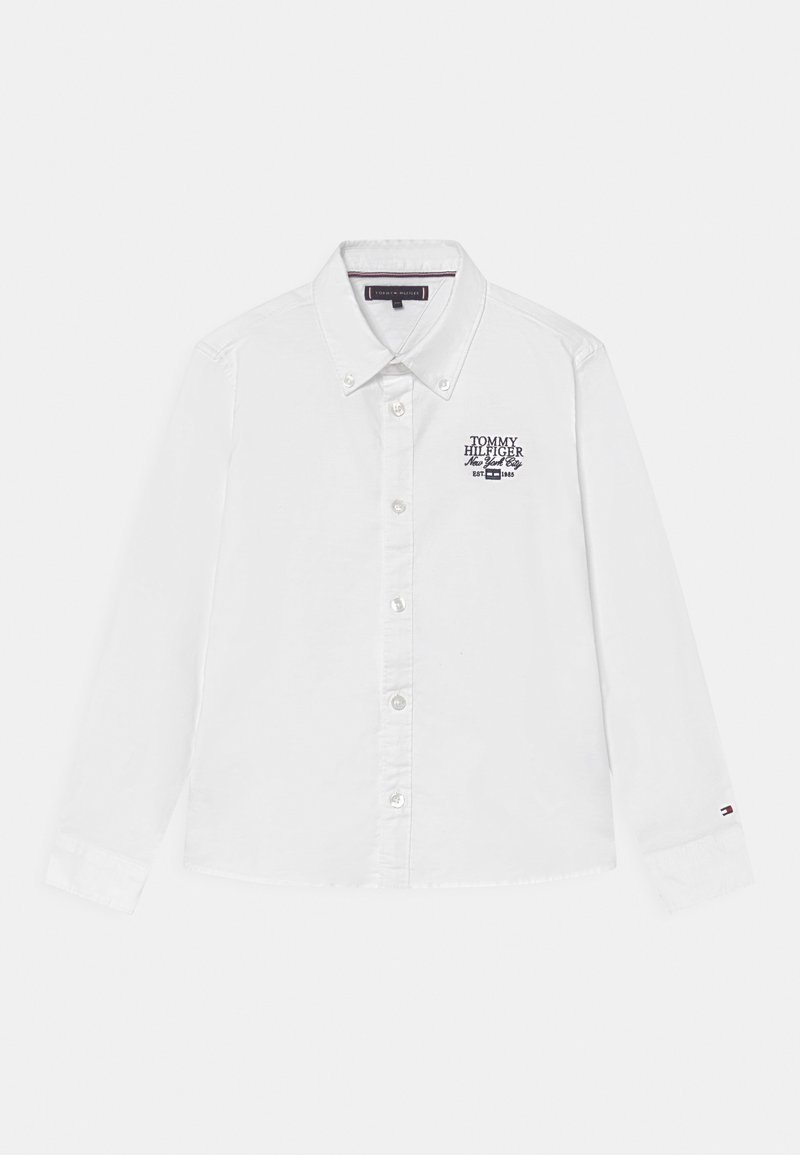 Chemise blanche à manches longues avec boutons, col boutonné, logo brodé "Tommy Hilfiger New York City" sur la poitrine et logo drapeau sur le poignet gauche.