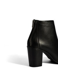 Bottine en cuir noir avec un bout arrondi, fermeture éclair latérale et un talon haut strié. Texture lisse avec une finition brillante.