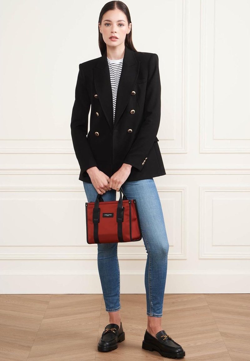 Blazer nero doppiopetto con bottoni dorati, t-shirt a righe, jeans blu, borsa rossa con dettagli neri e mocassini platform neri.