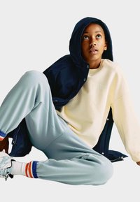 Námořnická kapucňová bunda přes krémovou mikinu s embosovaným textem, v kombinaci se světle modrými tepláky s multicolor ribbed manžetami.