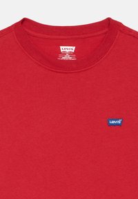 Κόκκινο βαμβακερό μπλουζάκι με στρογγυλή λαιμόκοψη, με μπλε λογότυπο Levi's ραμμένο στο αριστερό μέρος του στήθους. Απαλή υφή, μινιμαλιστικός σχεδιασμός.