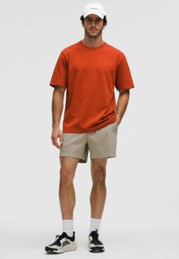 Camiseta de algodón roja, de corte holgado, combinada con pantalones cortos beige a rayas. Una gorra blanca y zapatillas negras con acentos claros completan el conjunto.