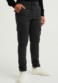 Mustat ja harmaan ruudulliset cargo-housut, joissa on sovitettu muotoilu, sivutaskut ja joustava vyötärö, yhdistettynä valkoisiin lenkkareihin.