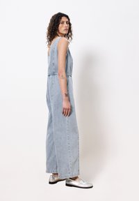 Lichtblauwe denim jumpsuit met wijde pijpen, schouderbanden en zijzakken. Gecombineerd met zilveren instappers. Textuurstof.