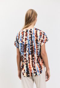Majica s kratkimi rokavi z vzorcem razpadajoče barve v oranžni, modri in črni barvi. Tkanina je videti lahka z ohlapnim krojem in zaobljenim robom.