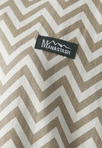 Woven fabric with a tan and white zigzag pattern; features a green label with "Manastash" and mountain graphic. Textured surface.
