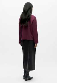 Bordeaux sweatshirt med lange ærmer, parret med en lang sort nederdel og sorte højhælede støvler, vist fra ryggen mod en hvid baggrund.