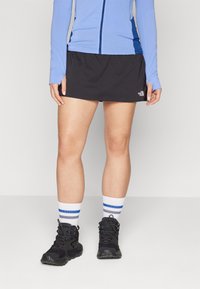 Svart kjol med ett strukturerat mönster, i kombination med en ljusblå långärmad topp. Svarta vandringskängor och vita strumpor med blå ränder fullbordar outfiten.